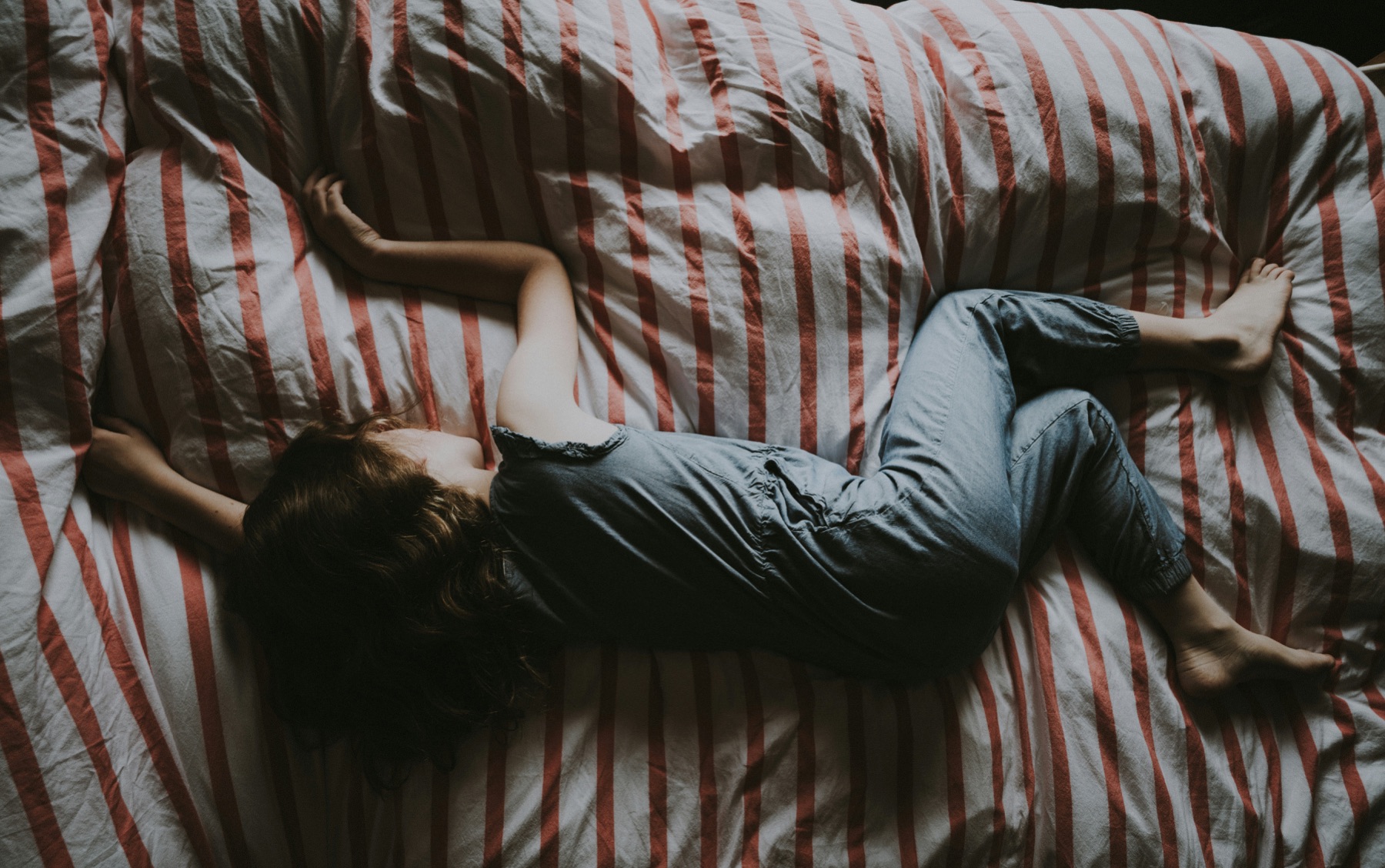 A child curled up asleep on a bed with red and white striped sheets