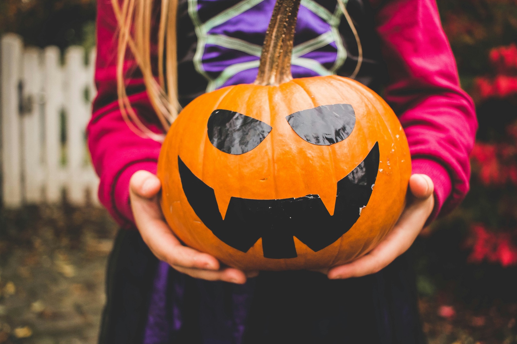 A child in a Halloween costume holding a jack-o'-lantern pumpkin